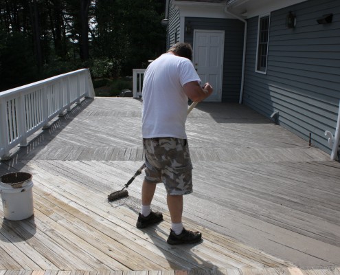 man applying armorrenew to wooden deck with roller and paint can